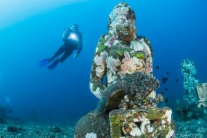 Taucher entdeckt mit Tauchlampe unterwasser eine Statue.